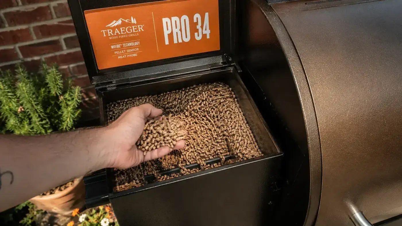 Pellet hopper of a Traeger Pro 34 open and full of hickory wood pellets, showing the auger feed system below